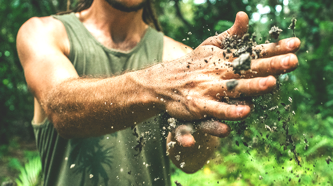 A man in a tank top has dirt in his hands.